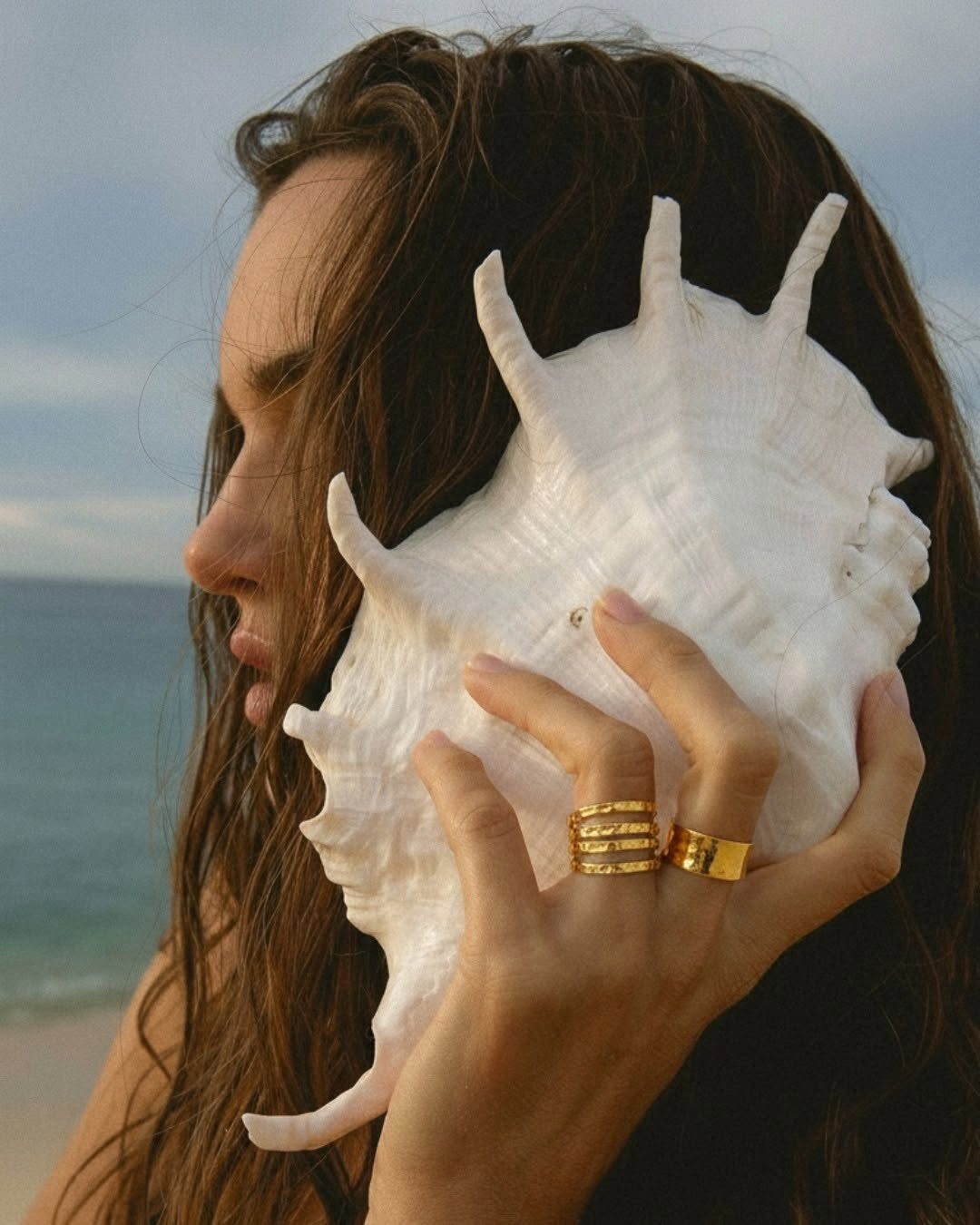 Femme tenant un coquillage, bagues dorées aux doigts